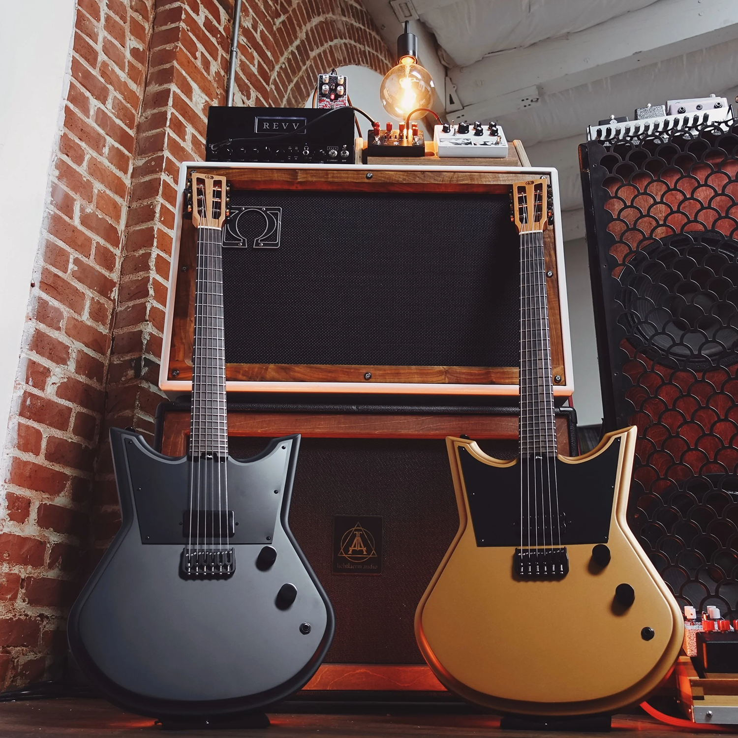 Two electric Kodex 6 string guitars in front of a guitar amplifier with brick wall background